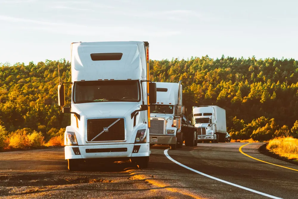 A white semi truck driving on a highway through a forested landscape